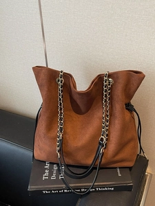Sac seau marron en daim avec bandoulière chaîne et cordon sur fond de livre minimaliste