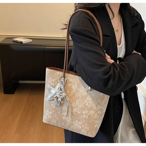 Detail of beige floral tote bag with brown leather strap and silver star pendant