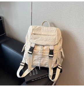Detail of cream nylon backpack featuring drawstring closure and black buckle straps