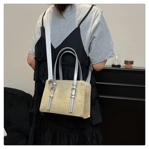 Detail of woven straw bag featuring silver leather handles and a wide nylon shoulder strap