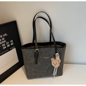 Detail of dark grey tote bag with matte leather texture and cute plush bear charm