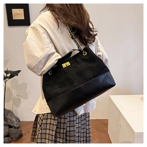 Detail of black suede and leather tote bag featuring diamond quilting and gold chain strap