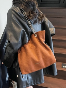 Sac seau en daim marron avec chaîne dorée porté avec une veste en cuir noir