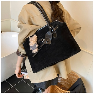 Detail of black suede and patent leather tote bag with a small teddy bear charm accessory