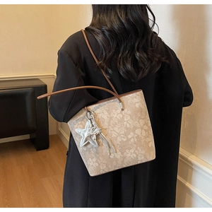 Detail of a beige floral tote bag with brown straps and a silver star charm accessory