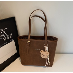 Detail of dark brown tote bag with metal buckles and a cute plush bear pendant accessory