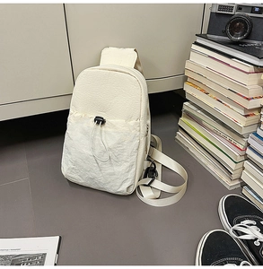 Detail of off-white sling bag with crinkled fabric texture and drawstring front pocket