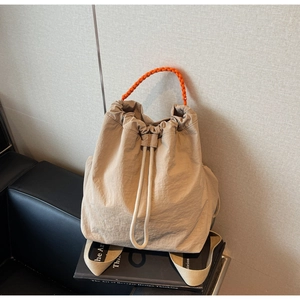 Dettaglio dello zaino in nylon beige con manico in tessuto arancione vivace sui libri