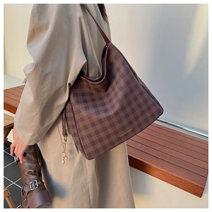Dettaglio di borsa hobo a scacchi marrone con scritte dorate e ciondolo di perle decorativo