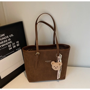 Detail of a brown suede tote bag with a cute plush bear and ribbon decoration