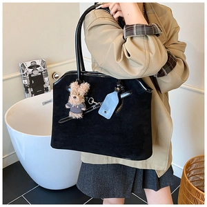 Detail of suede tote bag with shiny leather trim and cute bear charm shown on shoulder