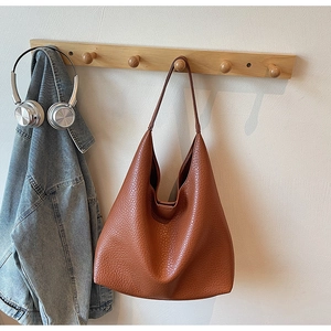 Detail of caramel brown litchi grain leather tote bag hanging on wooden rack