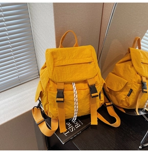 Detail of a bright yellow nylon backpack featuring buckle closures and a drawstring design
