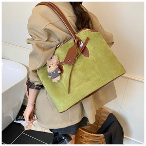 Detail of green suede tote bag with brown leather trim and cute teddy bear pendant