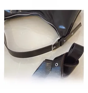 Detail showing silver zipper and adjustable strap on a dark brown glossy underarm bag