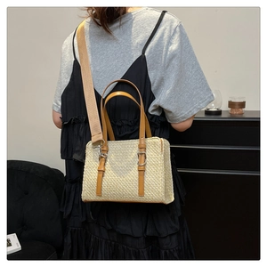 Detail of woven straw handbag with brown leather handles and wide fabric strap worn by model