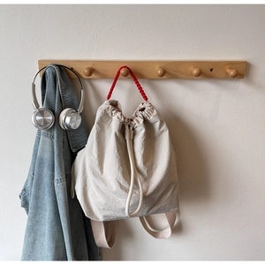 Detail of off-white drawstring backpack with red woven handle on a wooden rack