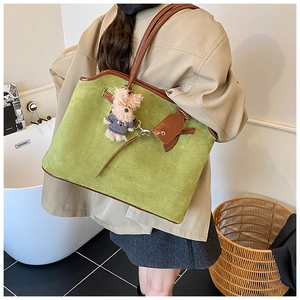 Detailed side view of green suede tote bag with brown leather handles and bear charm
