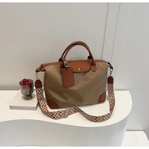 Detail of khaki nylon tote bag featuring brown leather handles and a woven shoulder strap
