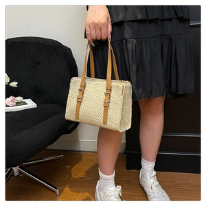 Detail of cream straw woven tote bag with brown leather straps and silver metal buckles