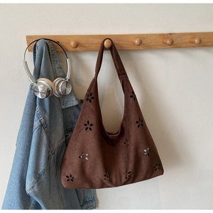 Detail of laser-cut floral pattern on deep brown suede hobo bag with wide shoulder strap