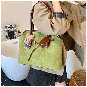 Close-up of green suede tote bag with brown leather handles and plush bear charm decoration