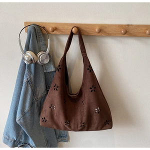 Hollow flower brown suede tote bag displayed on wooden hanger with denim jacket