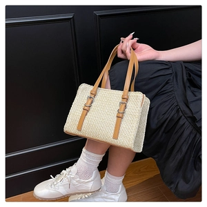 Detail of straw woven handbag with brown leather straps and metal buckle accents