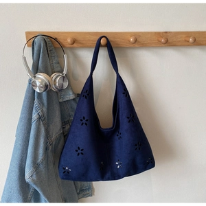 Close-up of laser-cut floral pattern on navy blue suede shoulder tote bag hanging on hook