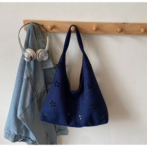Detail of dark blue hollow-out tote bag hanging on wooden hook with denim jacket