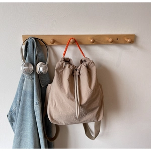 Detail of khaki drawstring backpack featuring vibrant orange braided top handle and nylon fabric