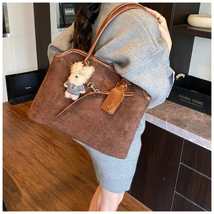 Detail of a large brown suede tote bag with a bear charm on a shoulder strap