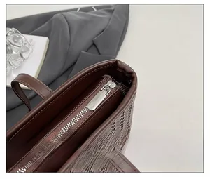 Close-up of the smooth silver zipper and woven leather texture on the brown tote bag
