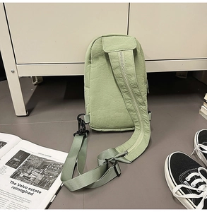Detail of sage green nylon chest bag with adjustable zipper strap on neutral ground