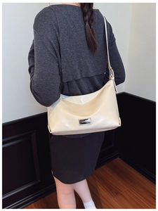 Close-up of cream glossy leather underarm bag with silver logo plate on a model