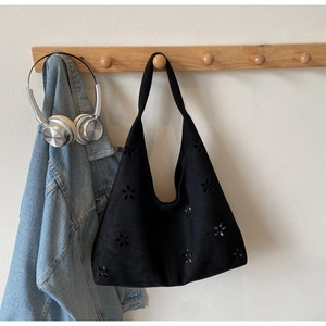 Detail of black suede hobo bag with laser-cut floral patterns on a wooden hanger