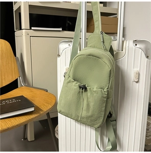 Light green nylon chest bag with drawstring pocket hanging on a suitcase handle