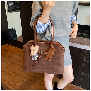 Detail of dark brown matte tote bag featuring teddy bear charm and sleek shoulder strap