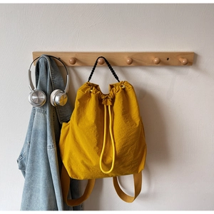 Detail of a bright yellow drawstring backpack made of waterproof nylon on a wooden hook