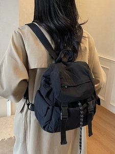 Minimalist black nylon backpack with flap and buckle closure shown on model's back
