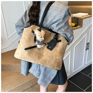 Rear view of a large khaki suede tote bag with teddy bear charm on a female model