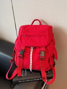Minimalist red nylon backpack with double buckles and woven drawstrings on a black book