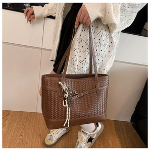 Detail of a brown woven tote bag featuring an intricate leather texture and unique side tassel