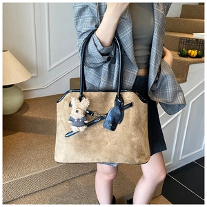 Detail of a large brown suede tote bag with black leather straps and bear charm