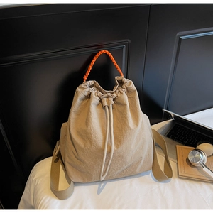 Dettaglio dello zaino in nylon beige con manico arancione su sfondo di biancheria da letto bianca