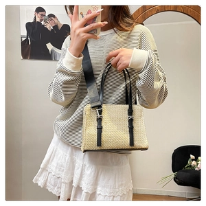 Mirror selfie showing woven straw shoulder bag with black PU handles and silver buckles