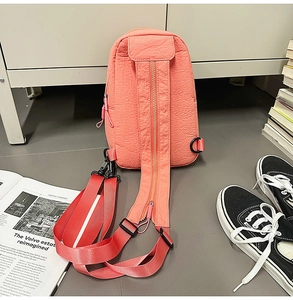 Detail of coral pink nylon chest bag featuring adjustable zipper shoulder straps