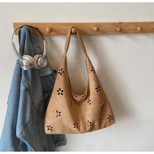 Detail of laser-cut floral pattern on brown suede tote bag in a casual setting