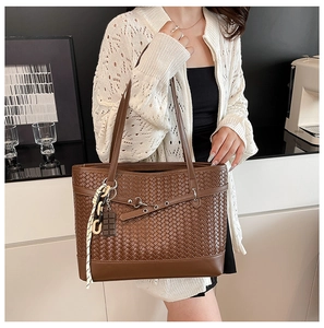 Detail of caramel woven tote bag with silk ribbon charm and chain accessory