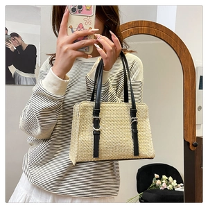 Detail of the woven straw texture and black leather handles on a casual beach crossbody bag
